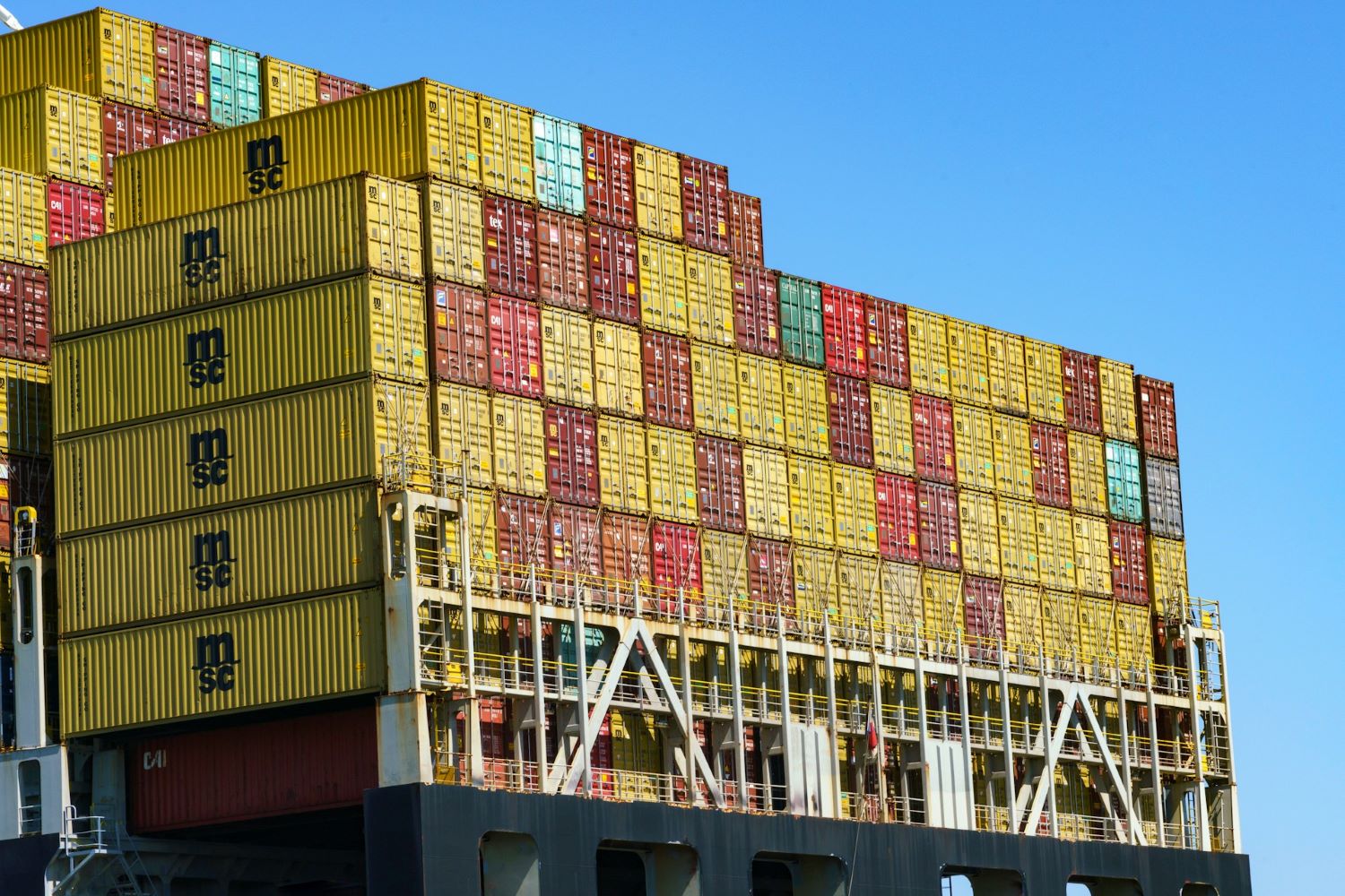 Lots of yellow and red international shipping containers stacked on top of each other against a blue sky.