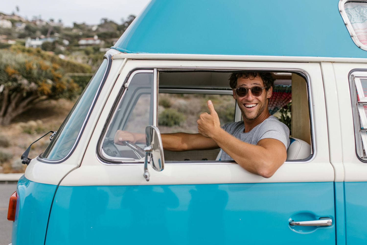 Smiling man in a blue campervan driving overseas with a CPD Carnet document.