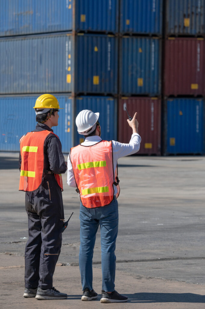 Two workers wearing high vis vests in a shipyard. Import cars from japan to australia.