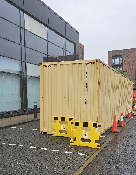 A shipping container on a pavement surrounded by cones, moved by container shipping companies using air freight and sea freight.