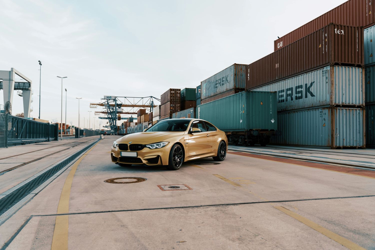 A close up of a gold car with shipping containers in the background. car shipping to australia.
